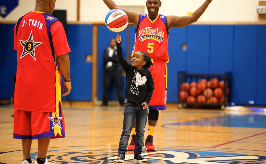 Harlem Wizards assisting young girl learn a basketball trick.