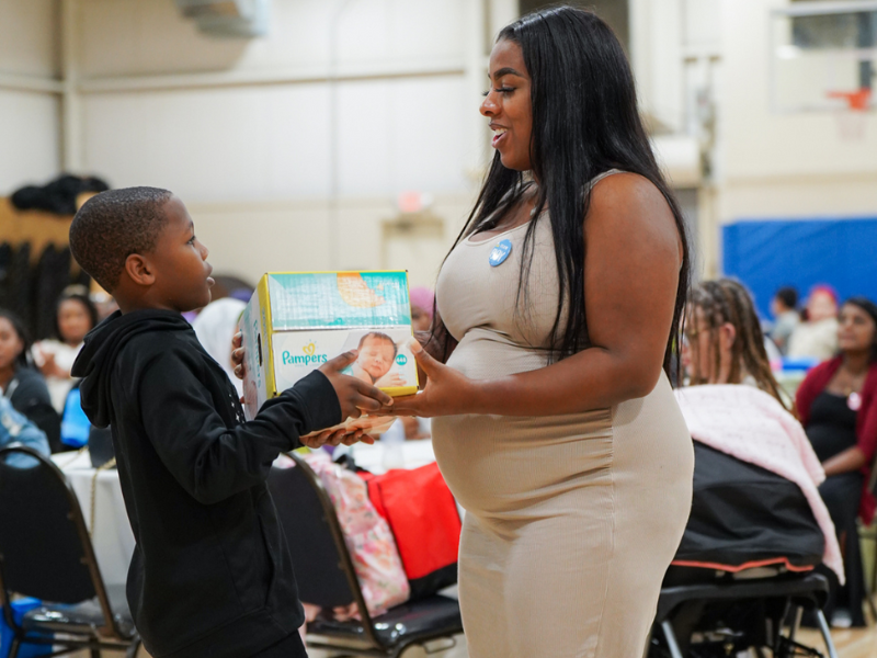 Small boy handing woman a box of diapers at Mint To Be of the Carolinas babyshower